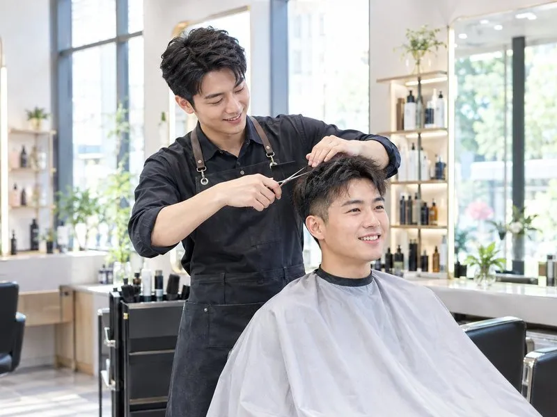 A barber cutting a customer's hair in a bright modern hair salon in China, illustrating how to say haircut in Chinese