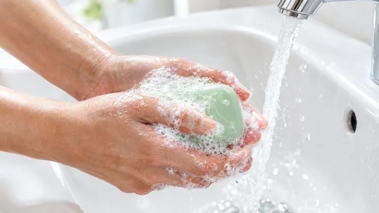 Soap in Chinese: hands lathering a bar of 肥皂 under running water at a bright white sink